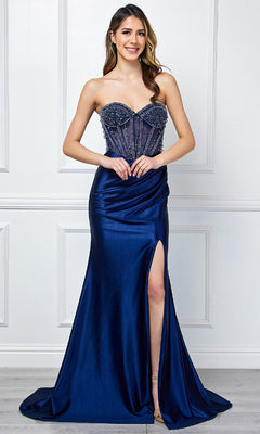 A woman stands against a white paneled wall in the Amelia Couture 4049 strapless long prom gown, featuring navy blue satin, a beaded bodice, sheer corset details, and a thigh-high slit.