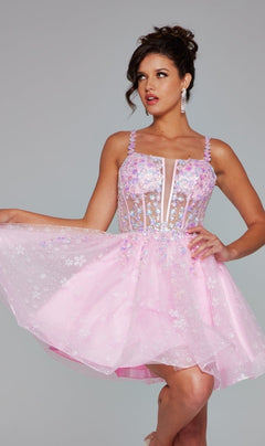 A woman models the Short Homecoming Dress 40501 by Jovani, a light pink A-line dress with floral sequin embroidery, sheer accents, and spaghetti straps, holding out the skirt against a plain gray background.