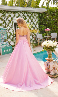 A woman in the Ava Presley 40523 long strapless prom dress stands by a pool, facing away, with greenery, flowers, and patio furniture in the background.
