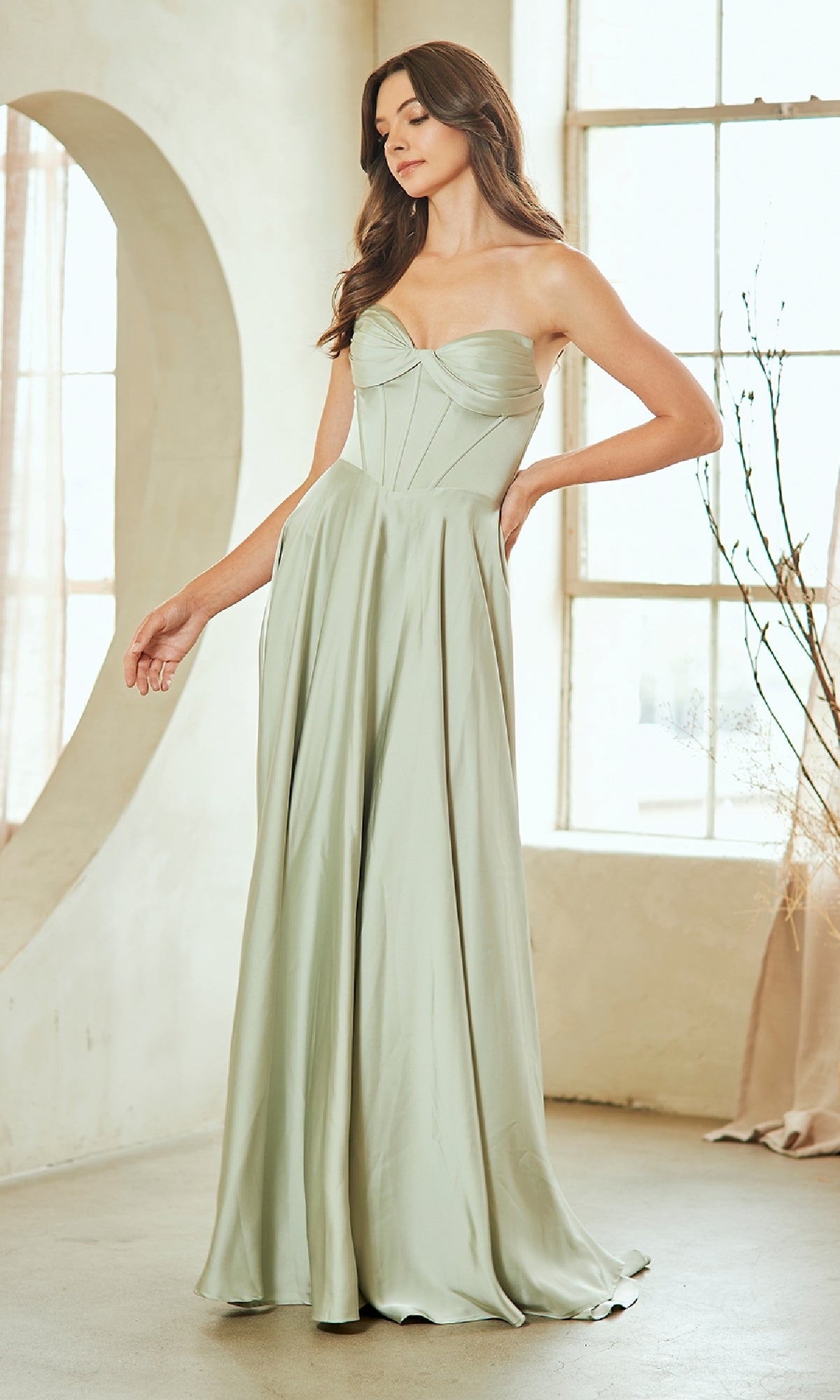 Woman wearing a light green strapless gown in a bright room with large windows.