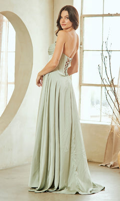 Woman showing the back of a light green evening gown with a lace-up design, standing in a bright room.