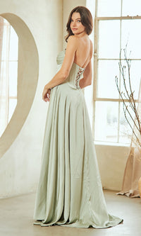 Woman showing the back of a light green evening gown with a lace-up design, standing in a bright room.
