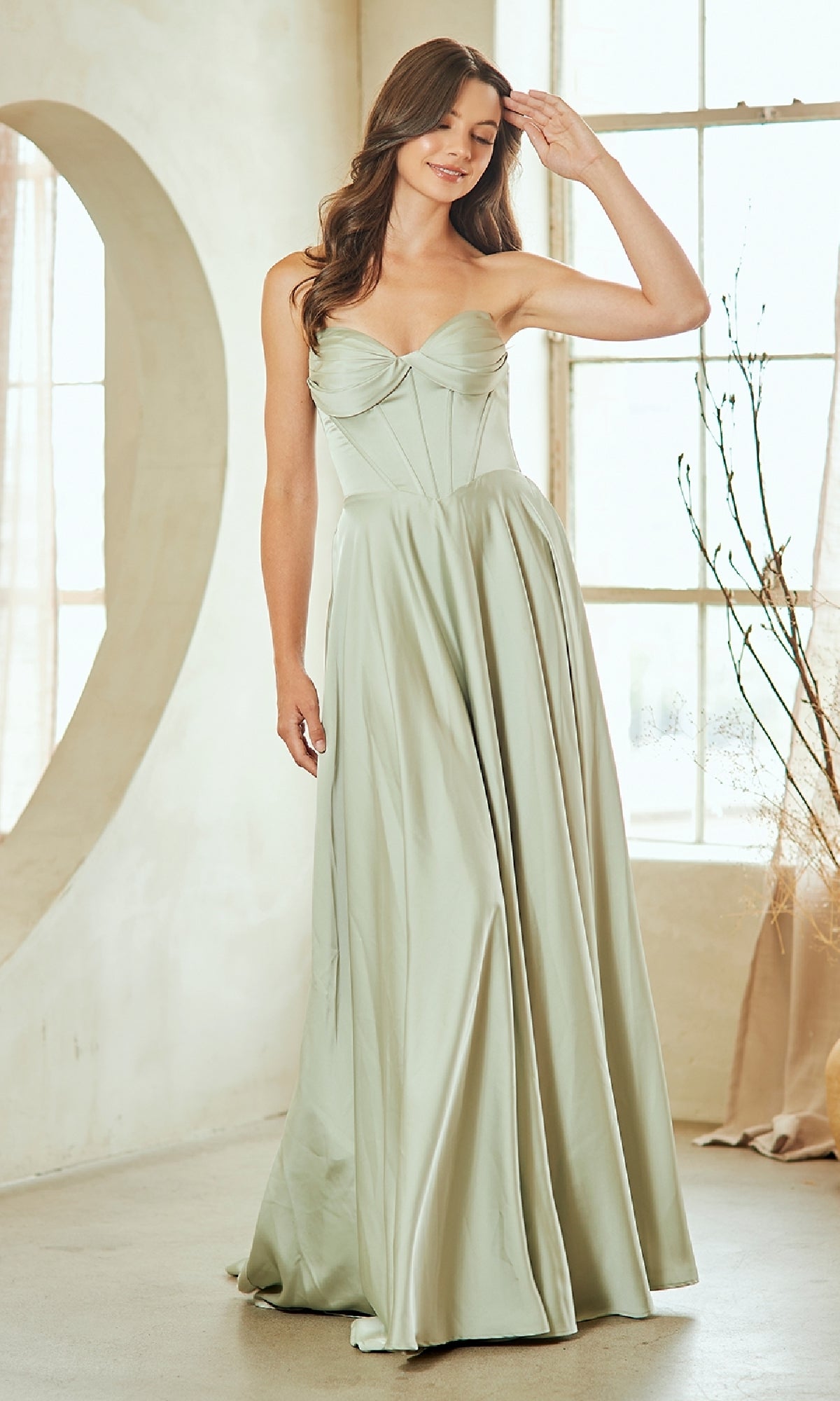 Woman wearing a light green strapless gown in a bright room with large windows.