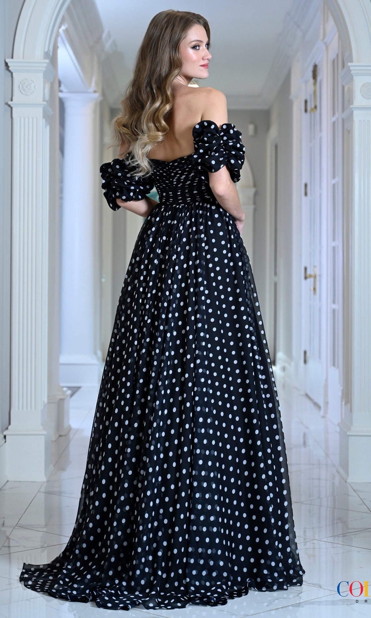 Woman wearing a vintage-inspired, off-the-shoulder black Long Prom Dress: Colors Dress 4053 with white polka dots and puffed sleeves.