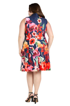 A woman showcases the back of the R&M Richards 4056W Plus-Size Wedding Guest Dress—a sleeveless, knee-length floral print dress—styled with black heeled sandals for a semi-formal look.