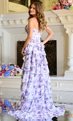 A person wears a Floral Corset Prom Dress: Colors Dress 4060, a floor-length, strapless floral chiffon corset dress with a white and purple print and a tiered ruffled skirt.