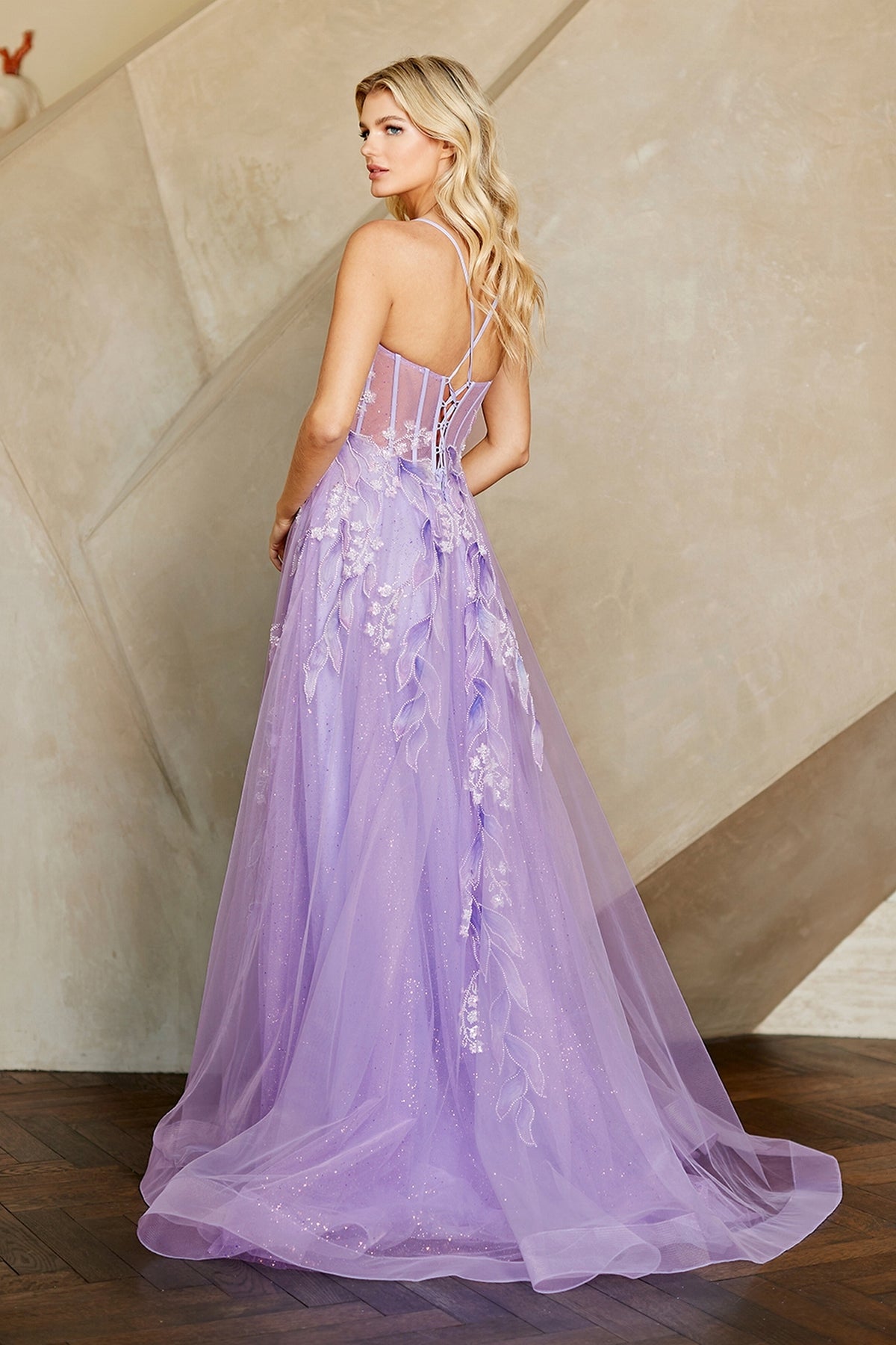 A person wearing the Long Prom Dress: Amelia Couture 4073, a lilac A-line gown with a corset bodice, leaf appliqués, and a full glitter tulle skirt with a train.