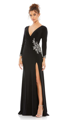 A woman wears the Long Formal Dress 41016 by Mac Duggal, featuring a fitted black design with a deep V-neck, silver floral embellishments, long sleeves, and a high leg slit, styled with silver high-heeled sandals.