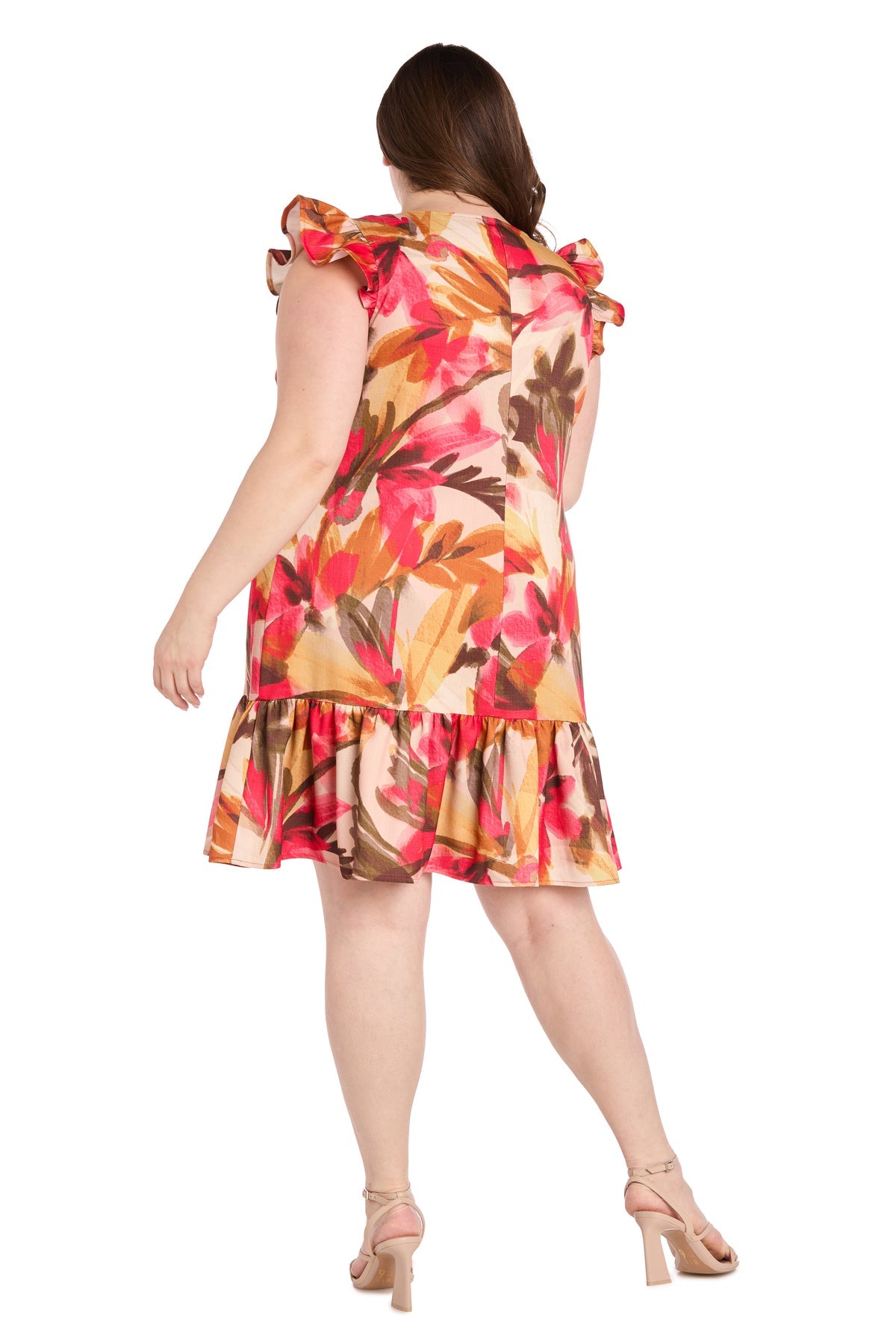 A woman wearing the Plus-Size Floral Party Dress: R&M Richards 4105W, a knee-length ruffle dress with a colorful floral pattern, stands with her back to the camera in nude heeled sandals.