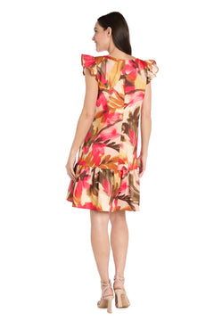 A woman faces away wearing the R&M Richards 4105P Petite Short Print Party Dress, featuring cap sleeves and a vibrant pink, orange, and brown floral print, paired with nude high-heeled sandals.