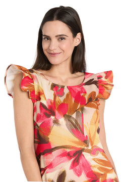 A woman wears the R&M Richards 4105P Petite Short Print Party Dress, featuring a sleeveless multicolored floral design with ruffled shoulders, while smiling at the camera against a white background.