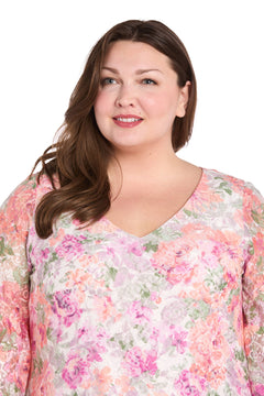 A woman with long brown hair, wearing the R&M Richards 4107W Plus-Size Print Party Dress, smiles and looks slightly to the side against a white background.