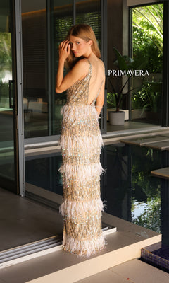 A woman stands by a modern glass door near an indoor pool, wearing the Primavera Long Beaded and Feathered Prom Gown 4132. The word "PRIMAVERA" is displayed beside her.