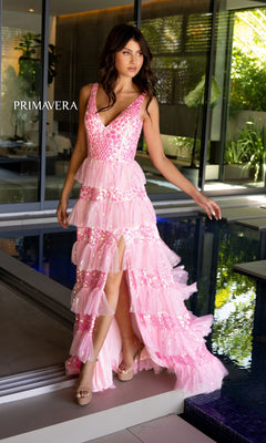 A woman stands by an indoor pool wearing the Primavera Tiered Long Beaded Prom Dress 4142, a sleeveless pink sequined dress with ruffled tiers and a high slit, set against modern décor and large windows for an elegant look.