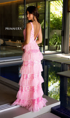 A woman stands by an indoor pool wearing the Primavera Tiered Long Beaded Prom Dress 4142, a floor-length, sleeveless gown with sequin details and a low back. The modern, well-lit space highlights its elegant sparkle.