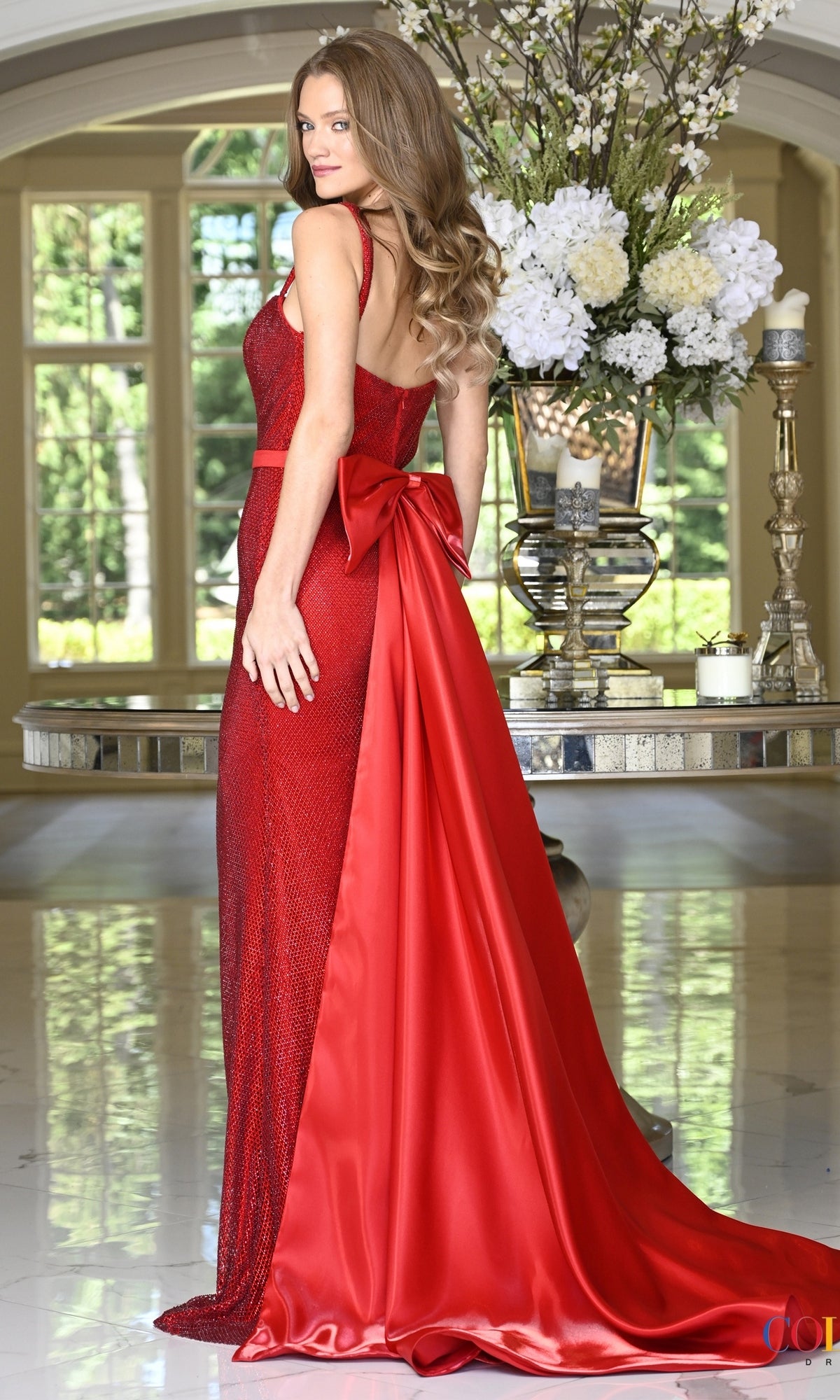 Colors Dress 4146 is a floor-length, shimmering red rhinestone mesh evening gown with a fitted bodice, thin straps, and a large satin bow at the back that flows into a train.