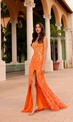 A woman stands outdoors near arched columns and greenery wearing the Primavera Ombre-Beaded Long Formal Gown 4150, a bright orange sequin prom dress with a thigh-high slit.