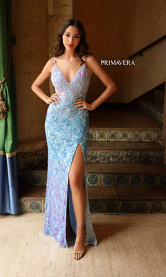 A woman stands indoors beside tiled stairs wearing the Primavera Ombre-Beaded Long Formal Gown 4150, a light blue ombre evening dress adorned with sequins and featuring a thigh-high slit. "PRIMAVERA" is displayed next to her.