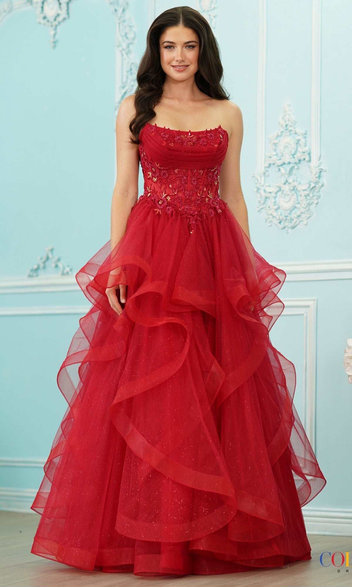A woman wearing a red Long Prom Dress: Colors Dress 4151, a strapless princess gown with a sweetheart neckline, lace corset bodice, and tiered, ruffled tulle skirt.