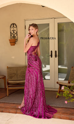 A woman in a sparkling magenta Primavera One-Shoulder Long Beaded Prom Dress 4152 stands on a patio, smiling as she faces away, with "PRIMAVERA" visible on the glass door behind her.