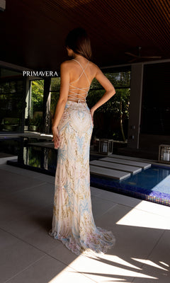 A woman stands by an indoor pool wearing the Primavera 4156 Beaded-Print Designer Prom Dress, which is floor-length and features intricate embroidery.
