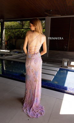 A woman stands by a pool wearing the Primavera 4156 Beaded-Print Designer Prom Dress with crisscross straps. "PRIMAVERA" appears on the wall in the background.