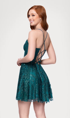 A woman with long red hair wears the Short Teal Glitter Hoco Dress (Blondie Nites 4159BN) featuring a lace-up strappy-back, smiling over her shoulder against a plain light background.