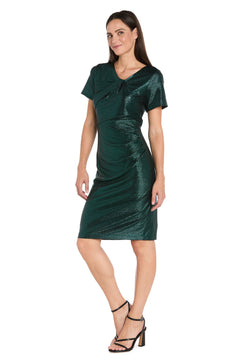 A woman poses against a plain white background wearing the R&M Richards 4177 short metallic cocktail dress in emerald green with short sleeves, paired with black high-heeled sandals.