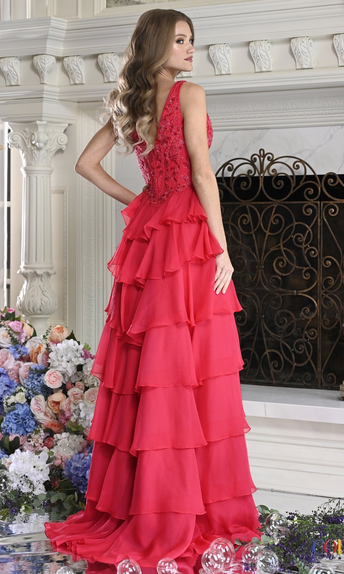 A woman wearing the red, floor-length Long Prom Dress: Colors Dress 4177, featuring a V-neck, a beaded, lace bodice, and a tiered, ruffled skirt.