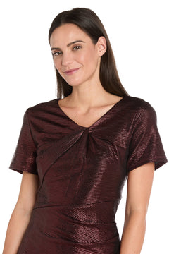 A woman with straight brown hair wears the R&M Richards 4177 short metallic cocktail dress in burgundy, smiling slightly while standing against a white background.