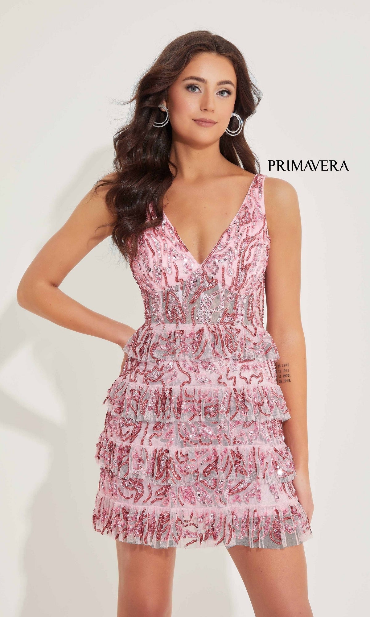 Woman models the sleeveless, V-neck Ruffled Short Sequin Hoco Dress (Primavera 4203) in pink with tiered ruffles, posing against a plain background with 