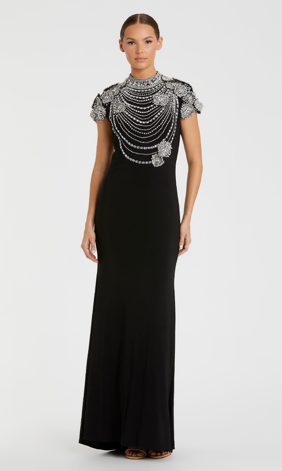 A woman wears the Mac Duggal 42055, a floor-length black formal dress with short sleeves, beaded details, and intricate silver embellishments on the shoulders and chest.
