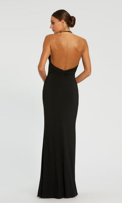 Woman in a Backless High-Neck Long Black Formal Dress 42065, standing with her hands behind her, facing away from the camera against a plain background.