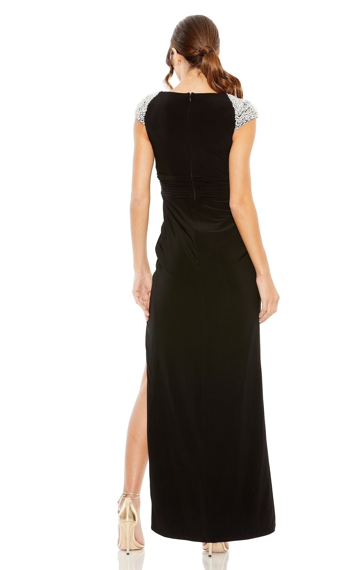 A woman stands with her back to the camera, wearing the Mac Duggal 42069 black formal evening gown featuring embellished cap sleeves and a ruched empire waistline.