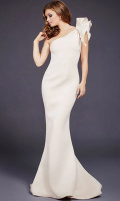 A woman poses against a plain dark background wearing the Jovani 32602 One-Shoulder Mermaid Prom Gown, a fitted, floor-length off-white dress featuring a single shoulder and a statement bow accent.