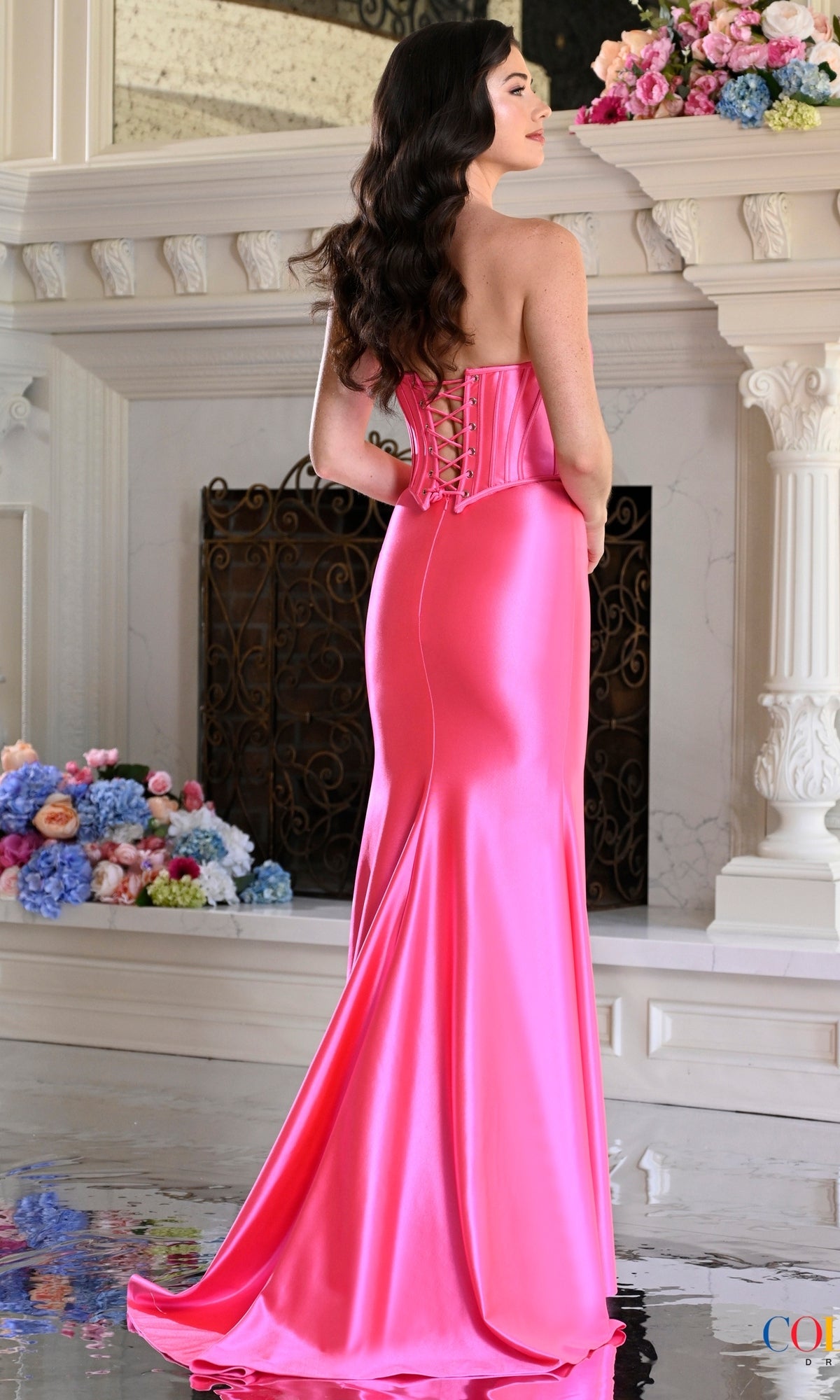 A person wearing a hot pink Long Prom Dress: Colors Dress 4208, a strapless, floor-length metallic jersey gown with a corset back.