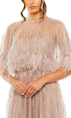 Woman wearing the Mac Duggal 42098 Feather-Cape Long Formal Dress, a blush-colored formal gown featuring sheer fabric, sequin embellishments, and feather details, stands with her hands together at her waist.