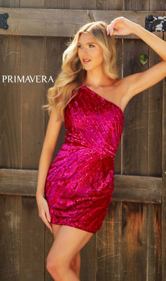 A woman poses outdoors in front of a wooden fence wearing the Primavera 4214 One-Shoulder Beaded Hoco Dress. The word "PRIMAVERA" appears on the left side of the image.