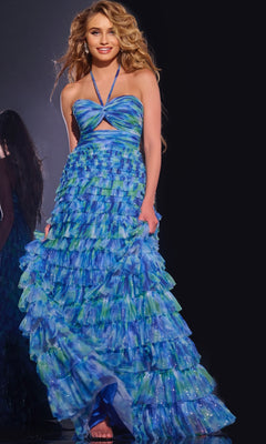 A woman stands barefoot against a dark background, smiling with loose wavy hair, wearing the Jovani 42182 Long Prom Dress in blue and green with tiered ruffles.