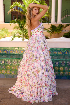 A woman in the Ava Presley 42208 long prom dress poses outdoors by a green tile wall, with palm trees and columns in the background.