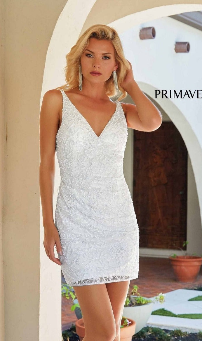 A woman wearing the Short Homecoming Dress 4225 by Primavera, a sleeveless v-neck style, stands before an arched doorway, gently touching her hair.