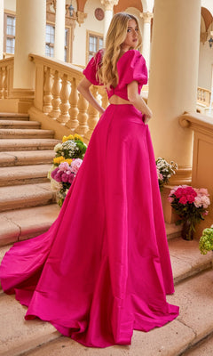 A woman wearing the Puff-Sleeve Long Prom Dress Ava Presley 42269 stands on stone steps lined with flower bouquets, looking over her shoulder.