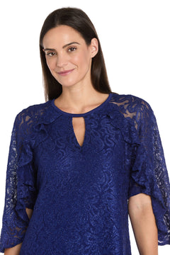 A woman with straight brown hair smiles slightly against a white background, wearing the R&M Richards 4226 Short Lace Semi-Formal Dress in royal blue, featuring ruffled sleeves and a keyhole neckline.