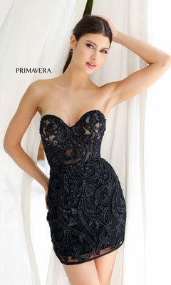A woman poses in the Strapless Beaded Short Hoco Dress: Primavera 4227, featuring intricate detailing, before white curtains. "PRIMAVERA" appears to the left.