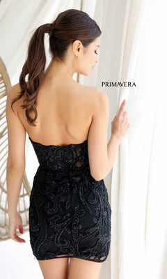A woman with medium-length brown hair in a ponytail models the strapless beaded short homecoming dress, Primavera 4227, standing with her back to the camera and looking over her shoulder. The word "Primavera" appears nearby.