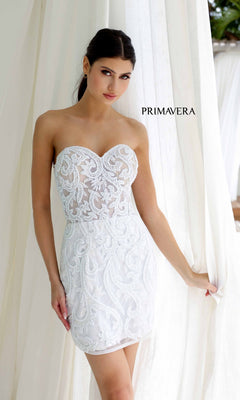 A woman in a white, strapless beaded short homecoming dress, Primavera 4227, stands by white curtains with "PRIMAVERA" printed beside her.
