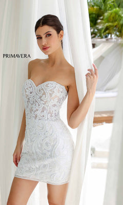 A woman stands by white curtains wearing the Strapless Beaded Short Hoco Dress, Primavera 4227—a fitted, strapless cocktail dress with lace patterns and beading; "PRIMAVERA" appears on the left.