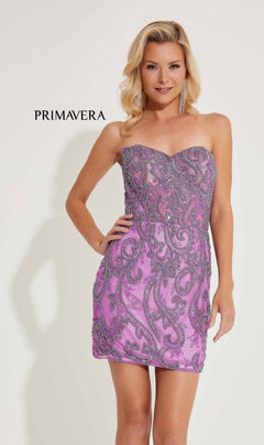 A woman poses in the Strapless Beaded Short Hoco Dress: Primavera 4227, a light purple short dress with silver sequin patterns; "Primavera" is displayed in the background.