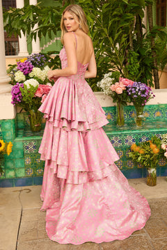 A woman stands outdoors by colorful tiles and lush plants, wearing the Ava Presley 42321 long prom dress—a backless, tiered A-line skirt gown.