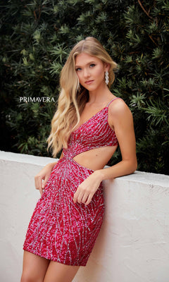 A woman wears the Short Homecoming Dress 4236 by Primavera, a fitted v-neck sequin mini dress with side cutouts, standing against a white wall with greenery in the background.